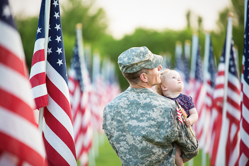 Veteran in Camo Holding Child in Field of Flags