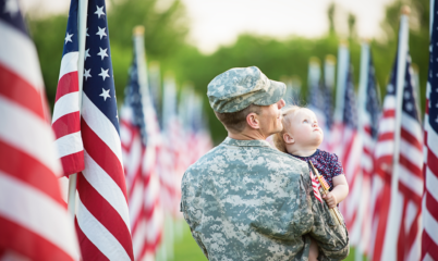 Veteran in Camo Holding Child in Field of Flags
